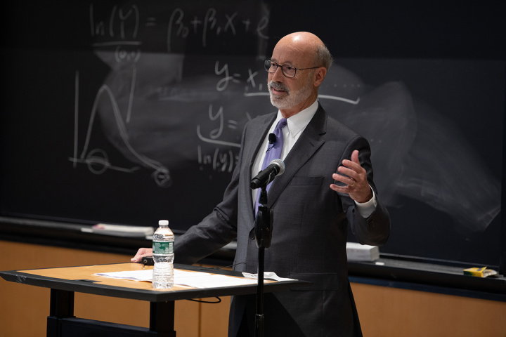 Pennsylvania Governor and MIT Political Science PHD alum Tom Wolf speaking in front of an chalkboard with problems sets written out