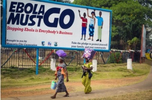 people walking by billboard that reads "Ebola Must Go"
