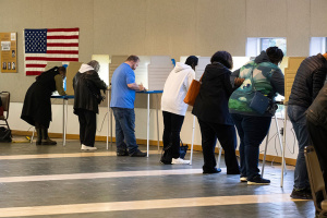 7 individuals voting with american flag draped on the wall to the side